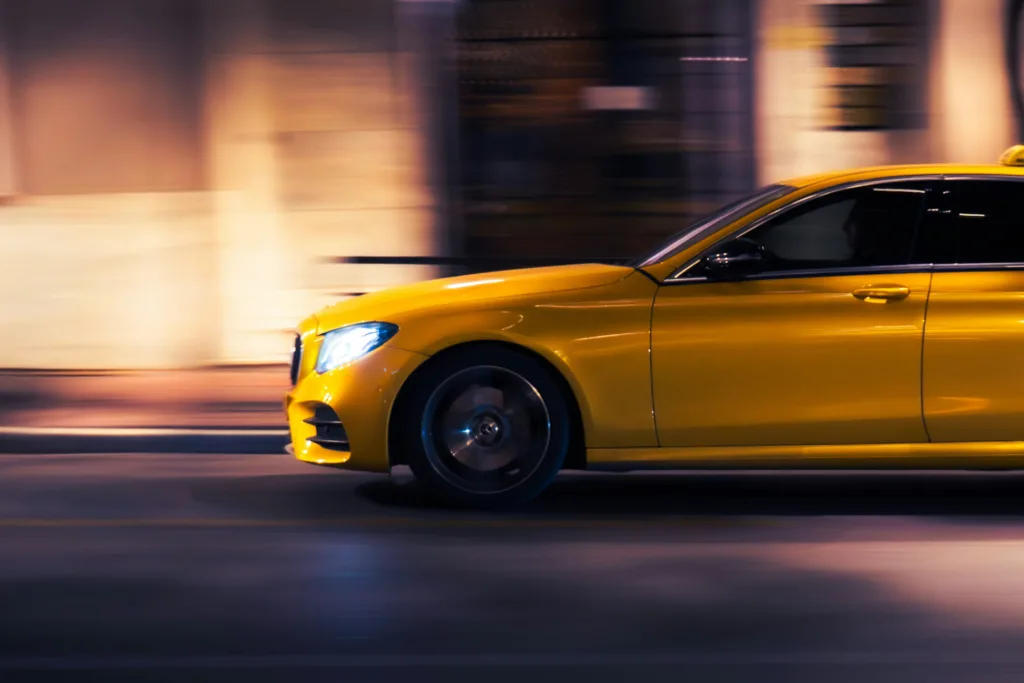A yellow car speeds down a city street at night.