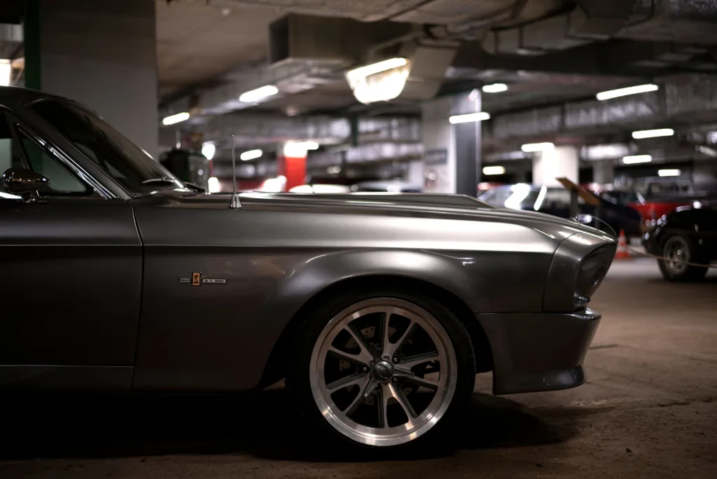 Close-up of a vintage gray car with stylish rims in an underground parking garage.