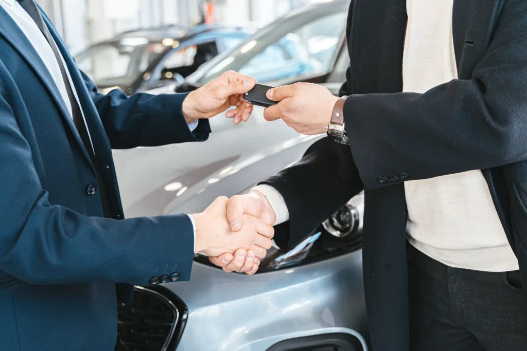 Two businessmen shaking hands and exchanging car keys in a dealership