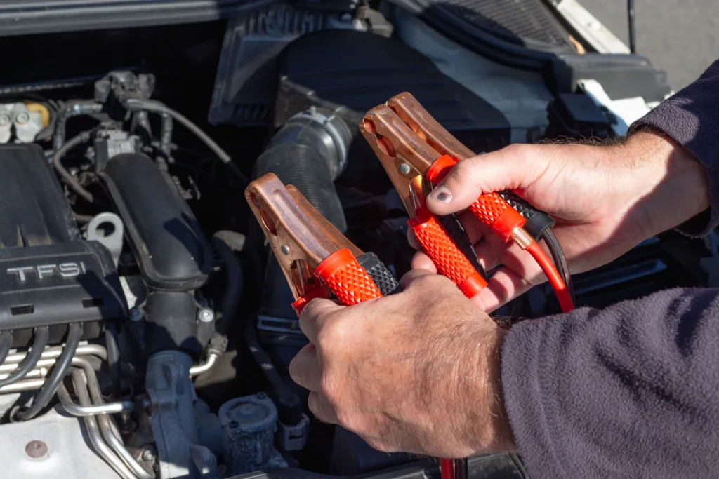 Close-up of hands holding jumper cables near a car engine