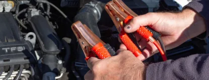 Close-up of hands holding jumper cables near a car engine