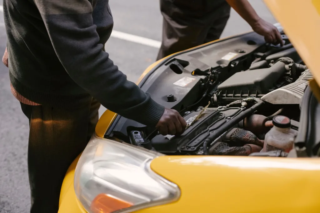 Two mechanics examining and fixing the engine of a yellow taxi cab on the road.