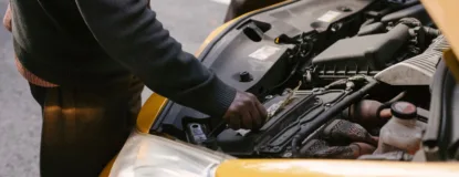 Two mechanics examining and fixing the engine of a yellow taxi cab on the road.